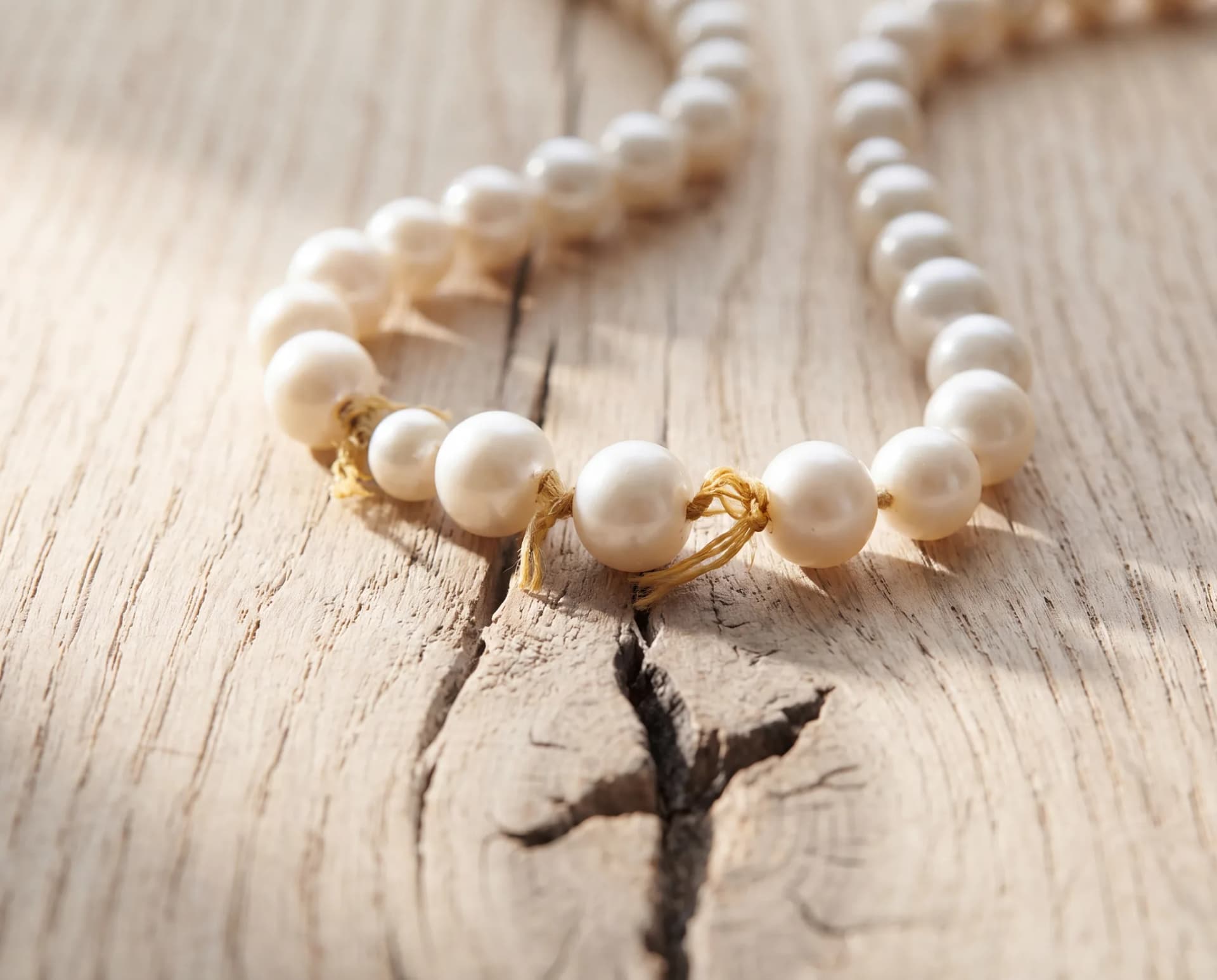 A pearl strand on a pale wood surface with visible gaps of stretched cord between several pearls
