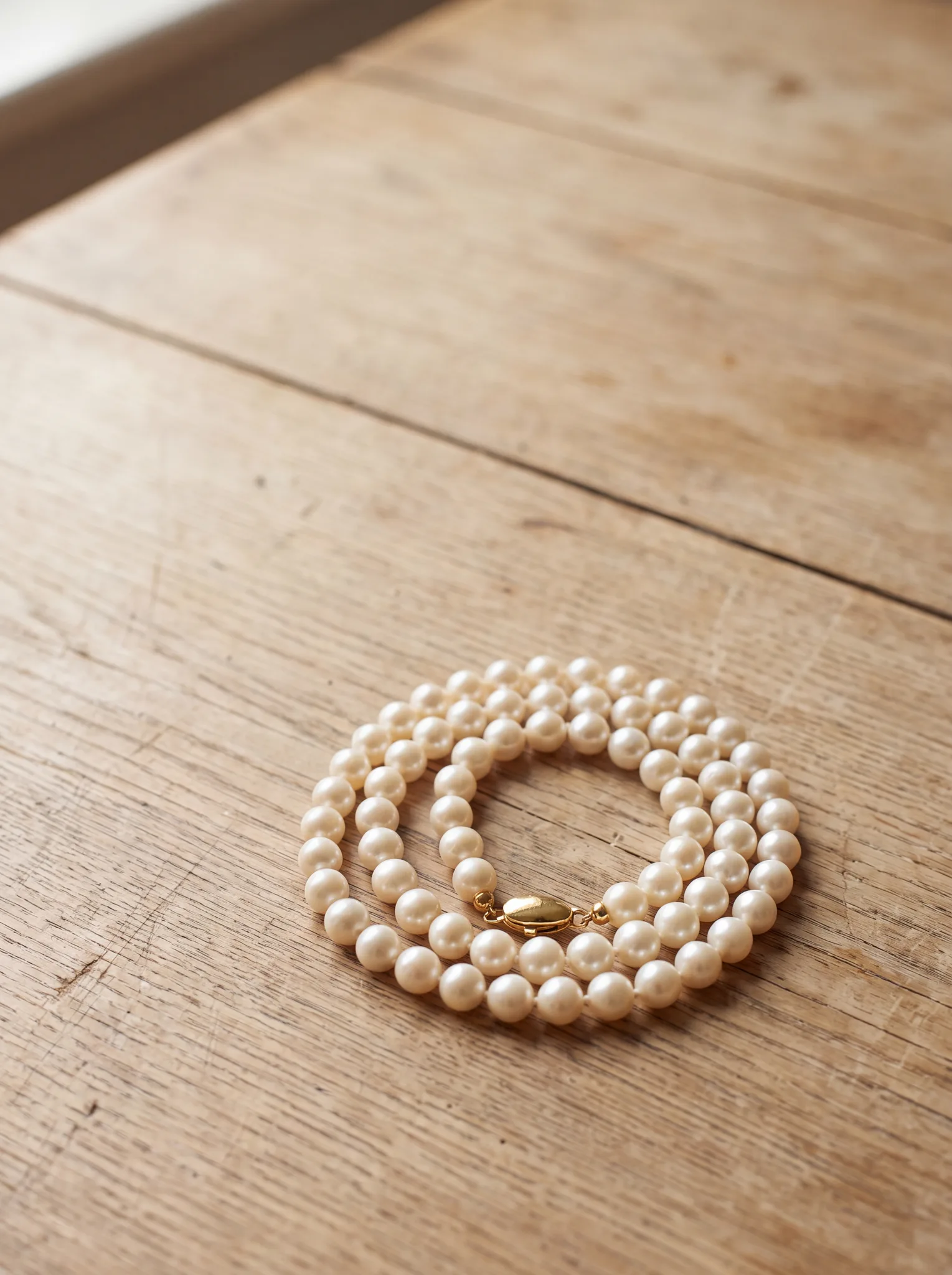 A knotted pearl strand with a gold clasp resting on a pale wood surface at ATL Luxury Jewelry, Snellville GA