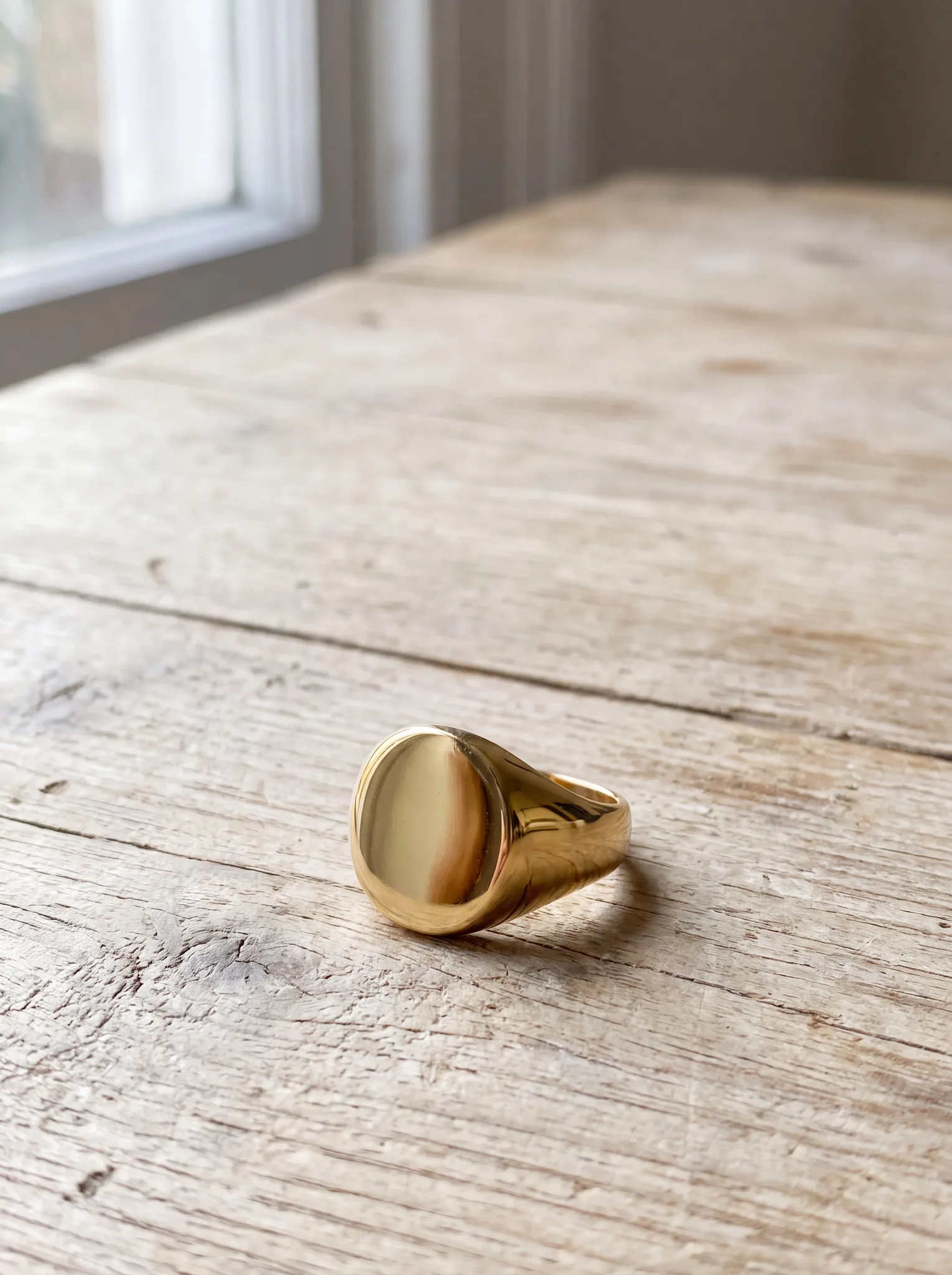 A polished yellow gold signet ring resting on a pale wood surface at ATL Luxury Jewelry, Snellville GA