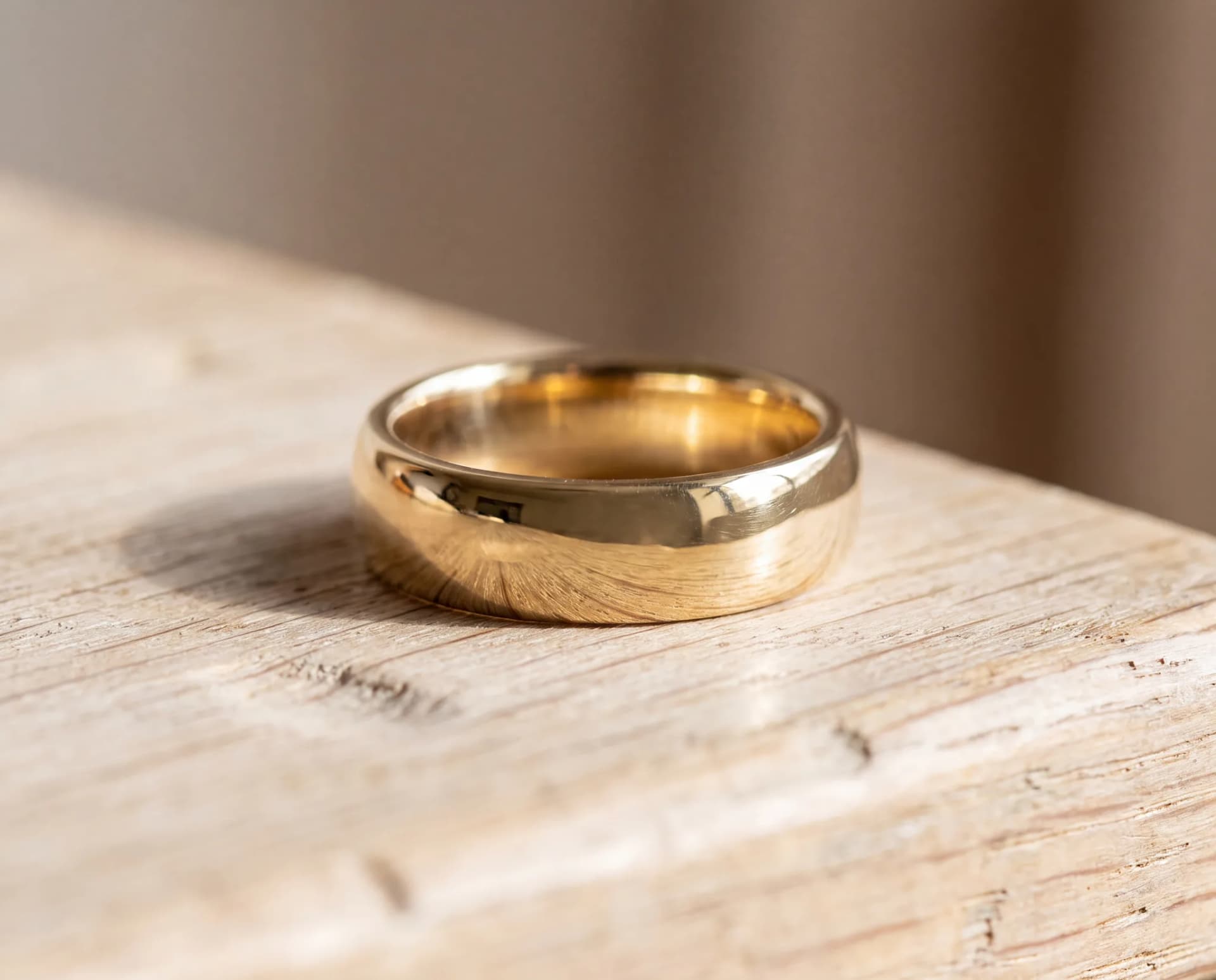 A freshly polished gold ring on a pale wood surface, bright with crisp highlights