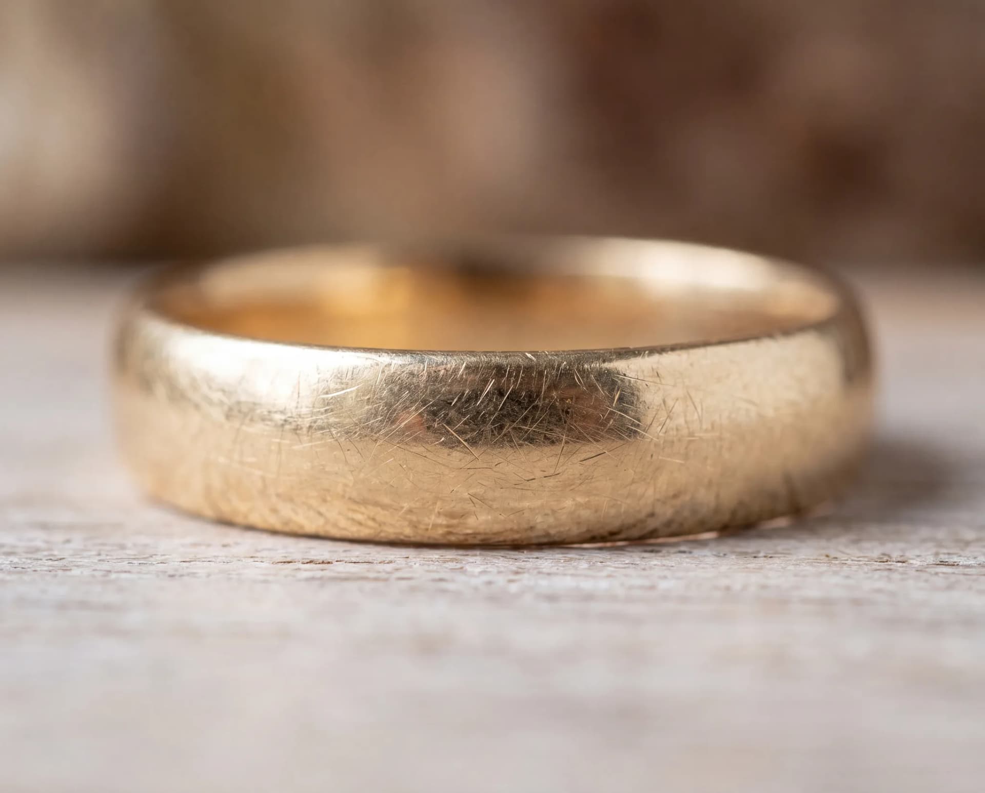 A macro view of a gold ring's surface on a pale wood surface covered in fine hairline scratches