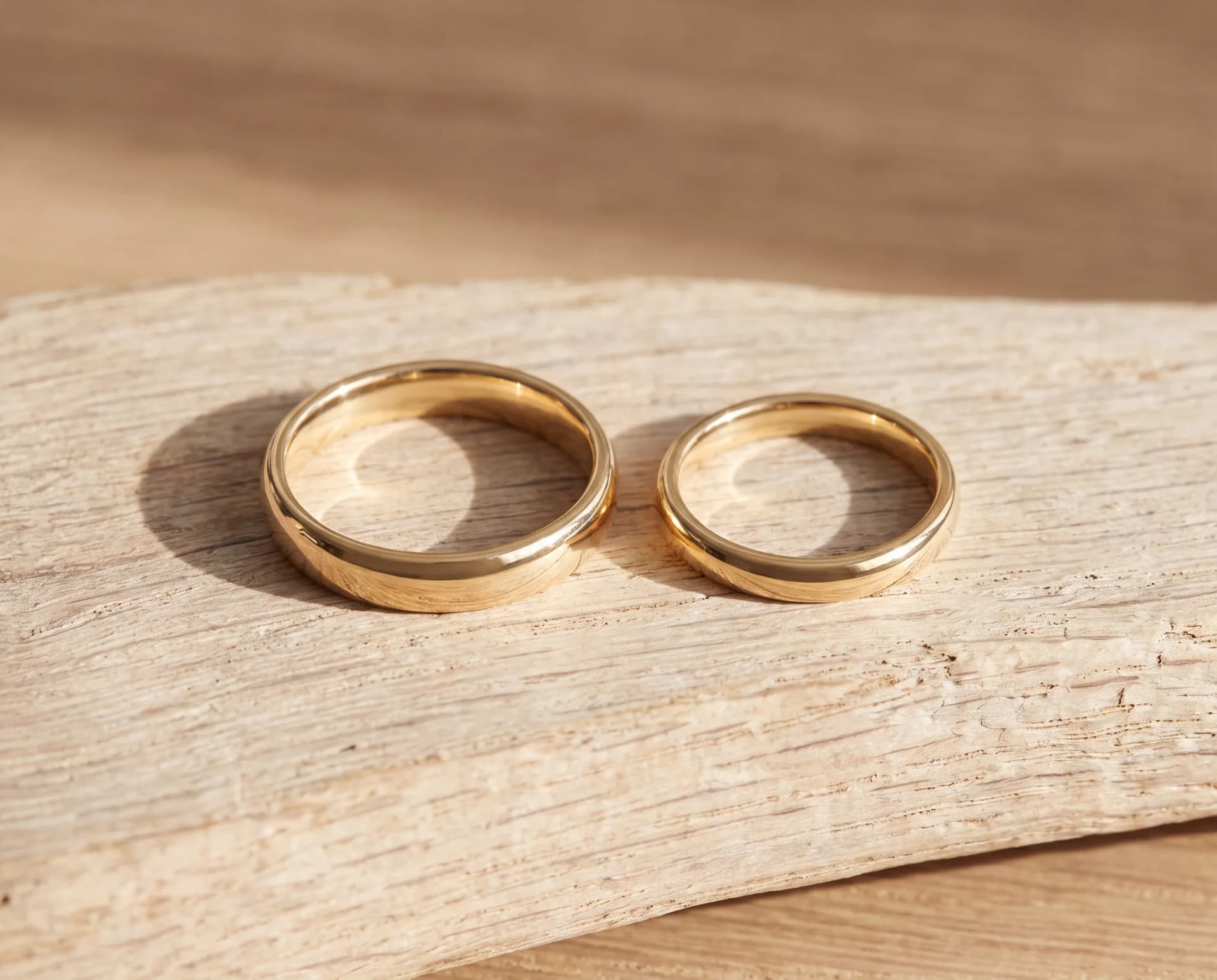 Two gold bands of different diameters lying side by side on a pale wood surface