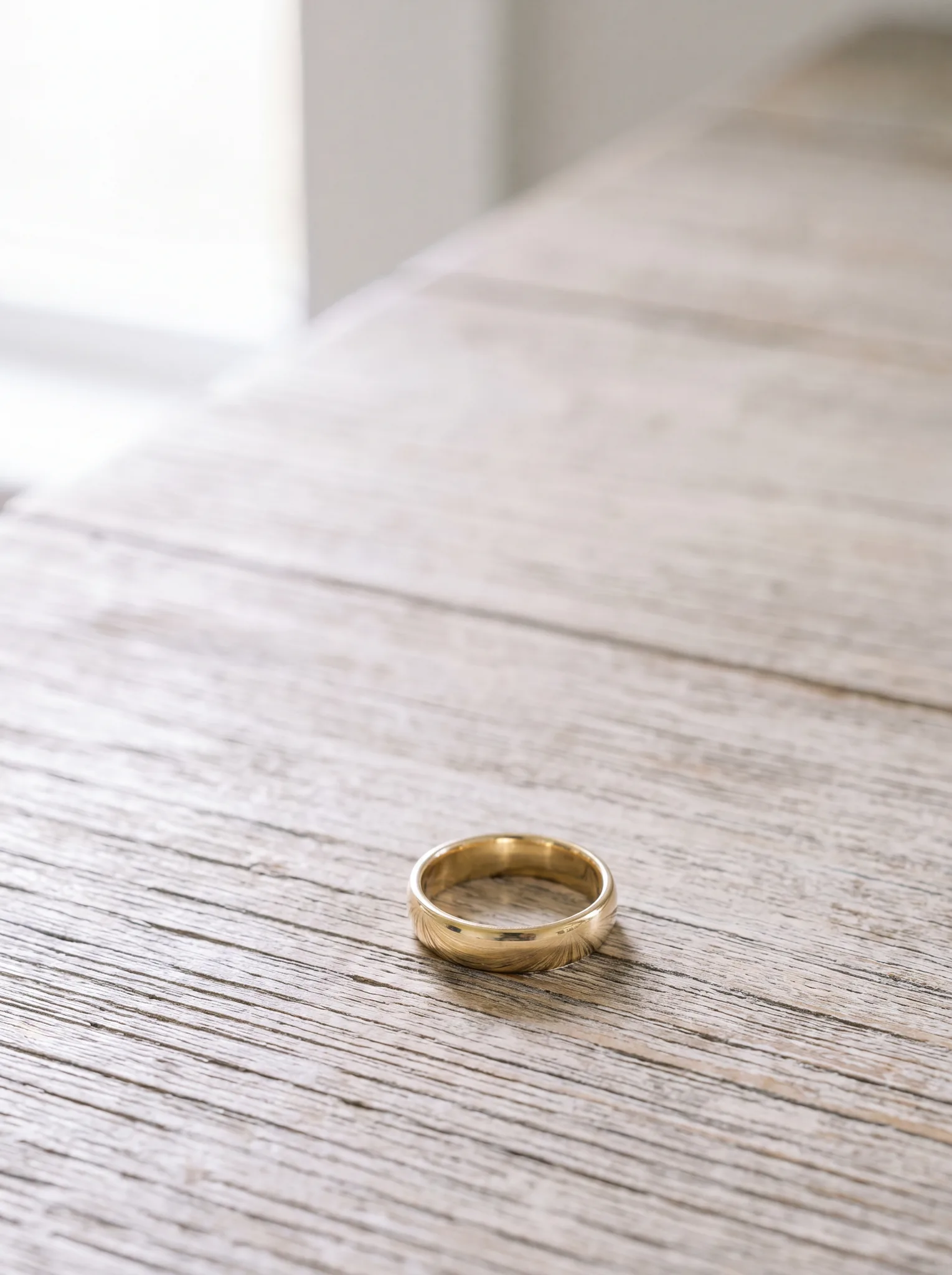 A plain yellow gold wedding band resting on a pale wood surface at ATL Luxury Jewelry, Snellville GA