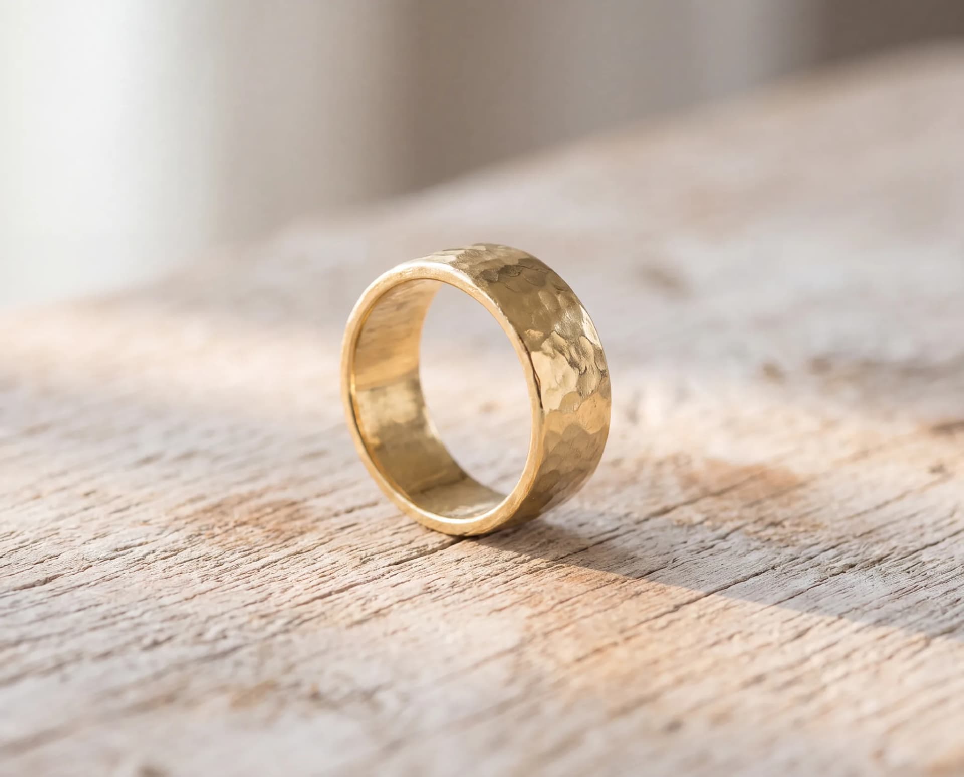 A wide loose gold band lying on its side on a pale wood surface