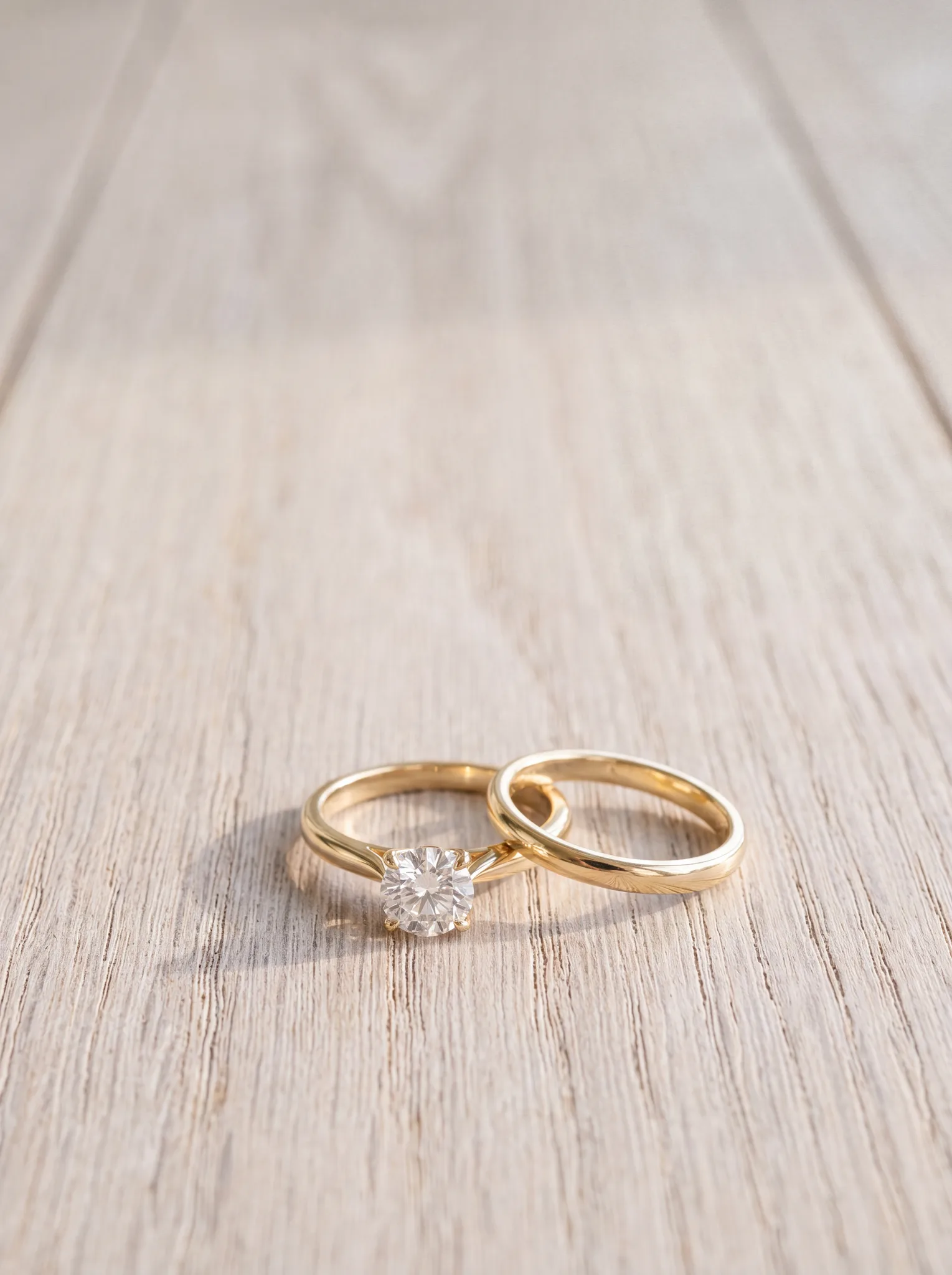 A yellow gold engagement ring and matching wedding band resting on a pale wood surface at ATL Luxury Jewelry, Snellville GA
