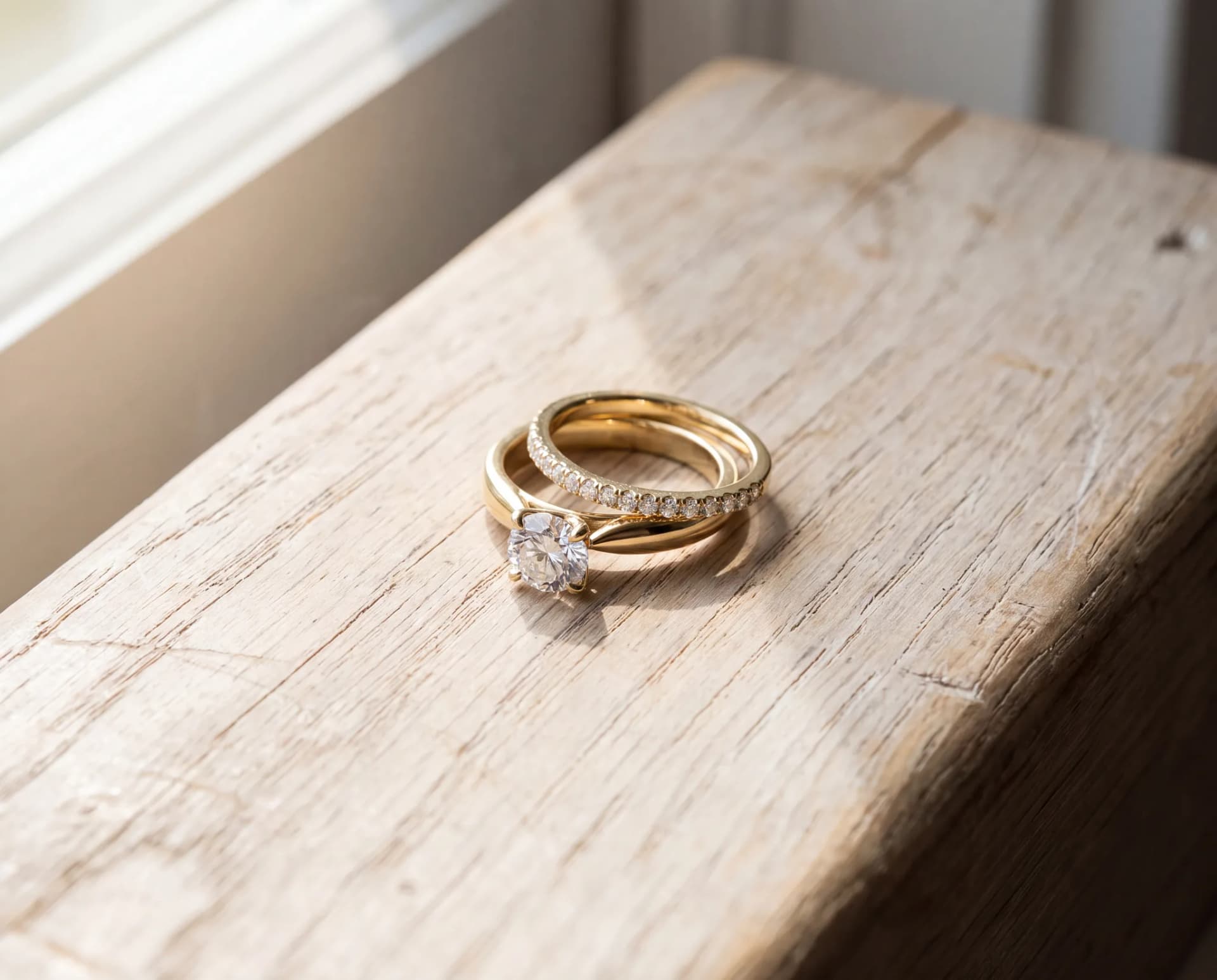 A gold engagement ring and wedding band nested flush together as a joined bridal set on a pale wood surface