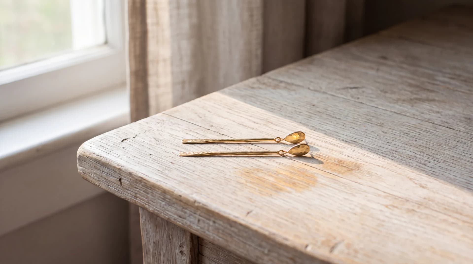 A pair of yellow gold drop earrings lying side by side on a pale wood surface