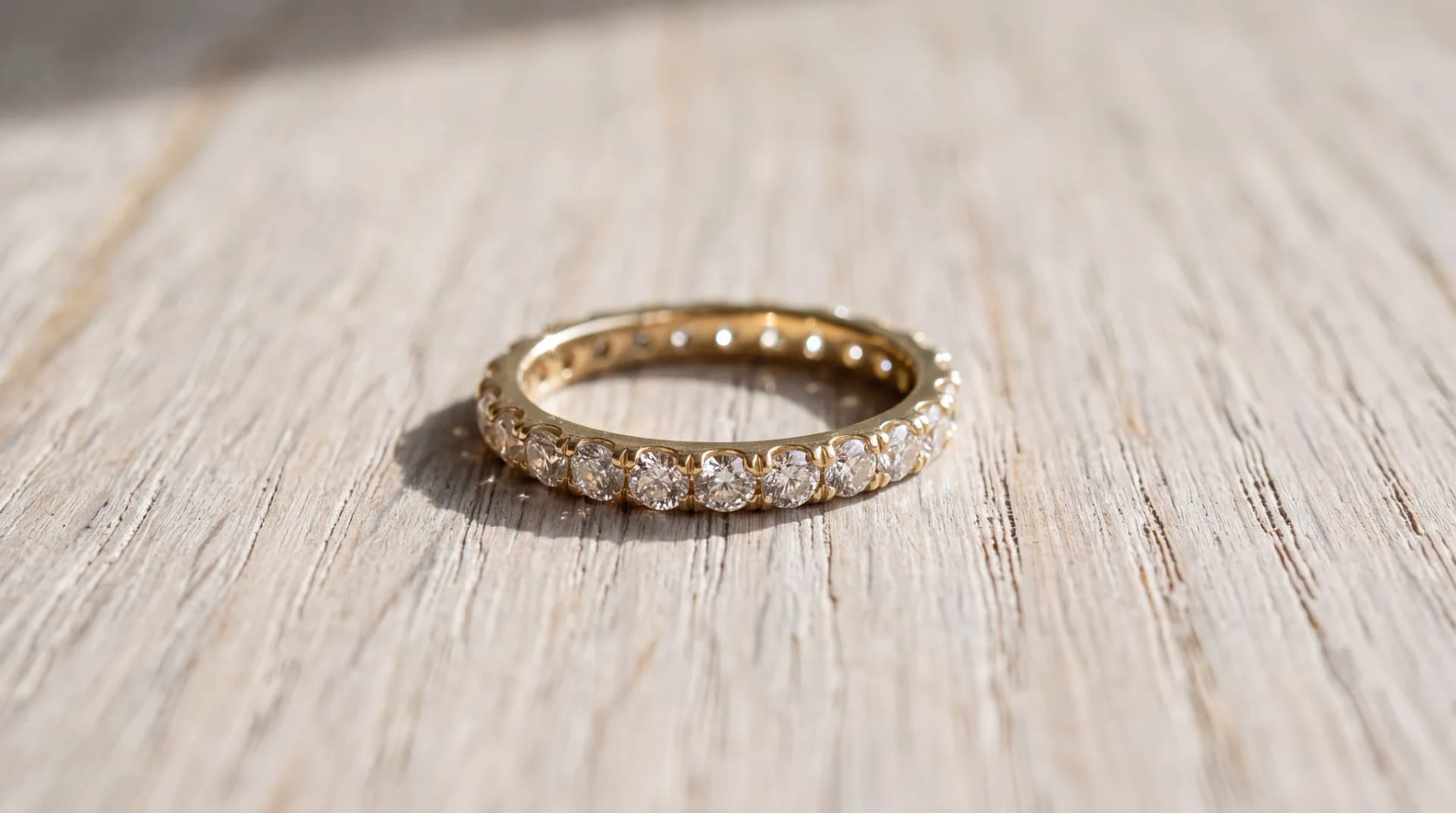 A yellow gold diamond eternity band lying on a pale wood surface