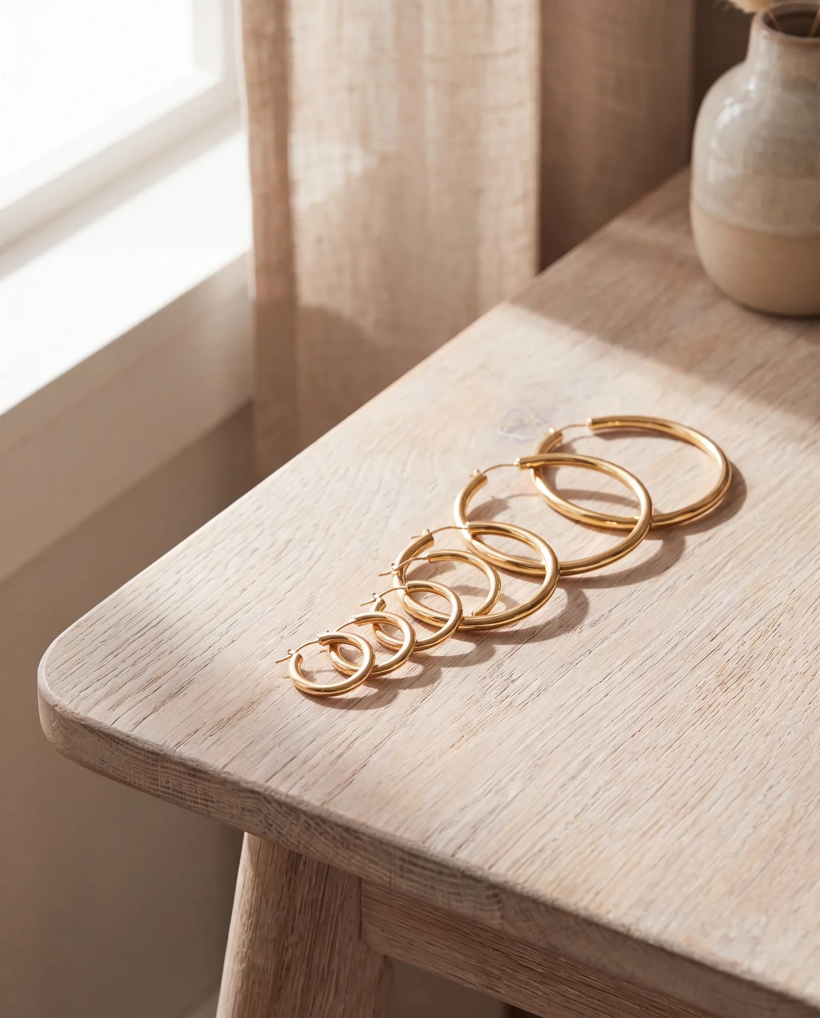 Several pairs of yellow gold hoop earrings in graduated sizes on a pale wood surface