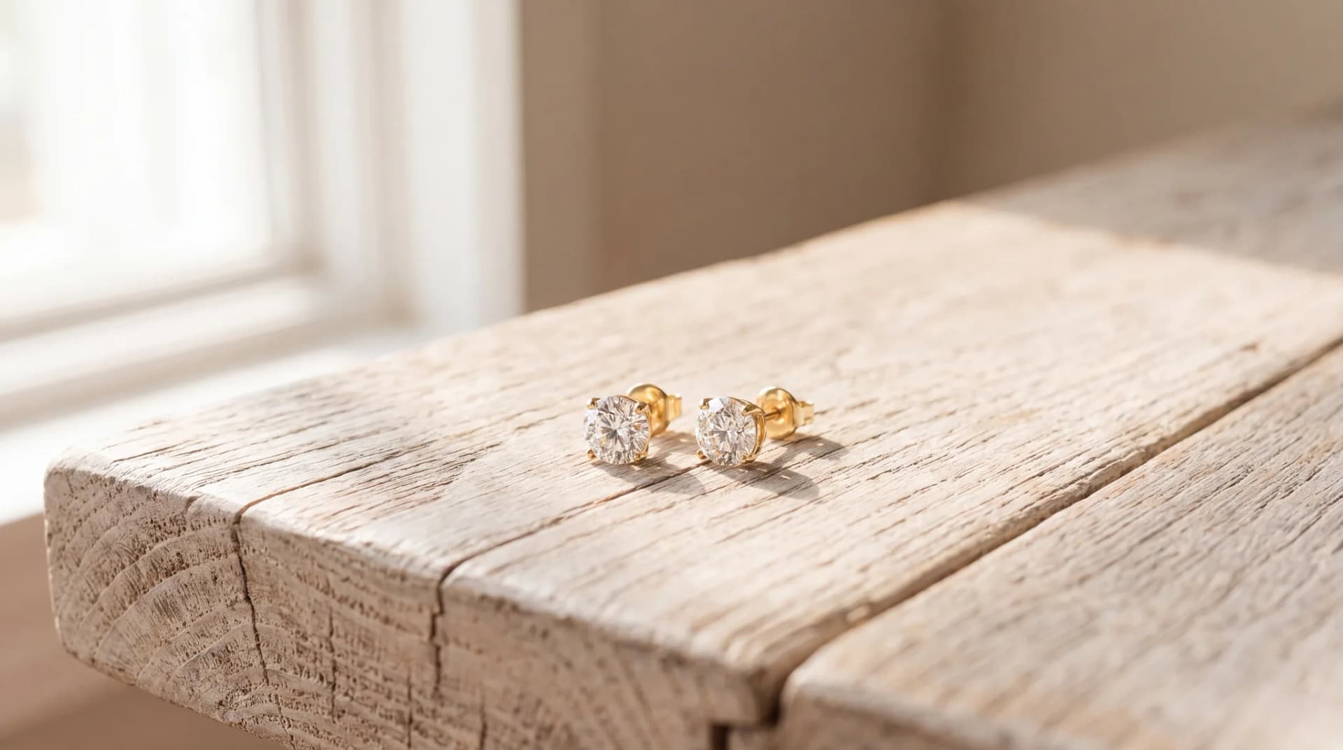 A pair of round diamond stud earrings in yellow gold on a pale wood surface