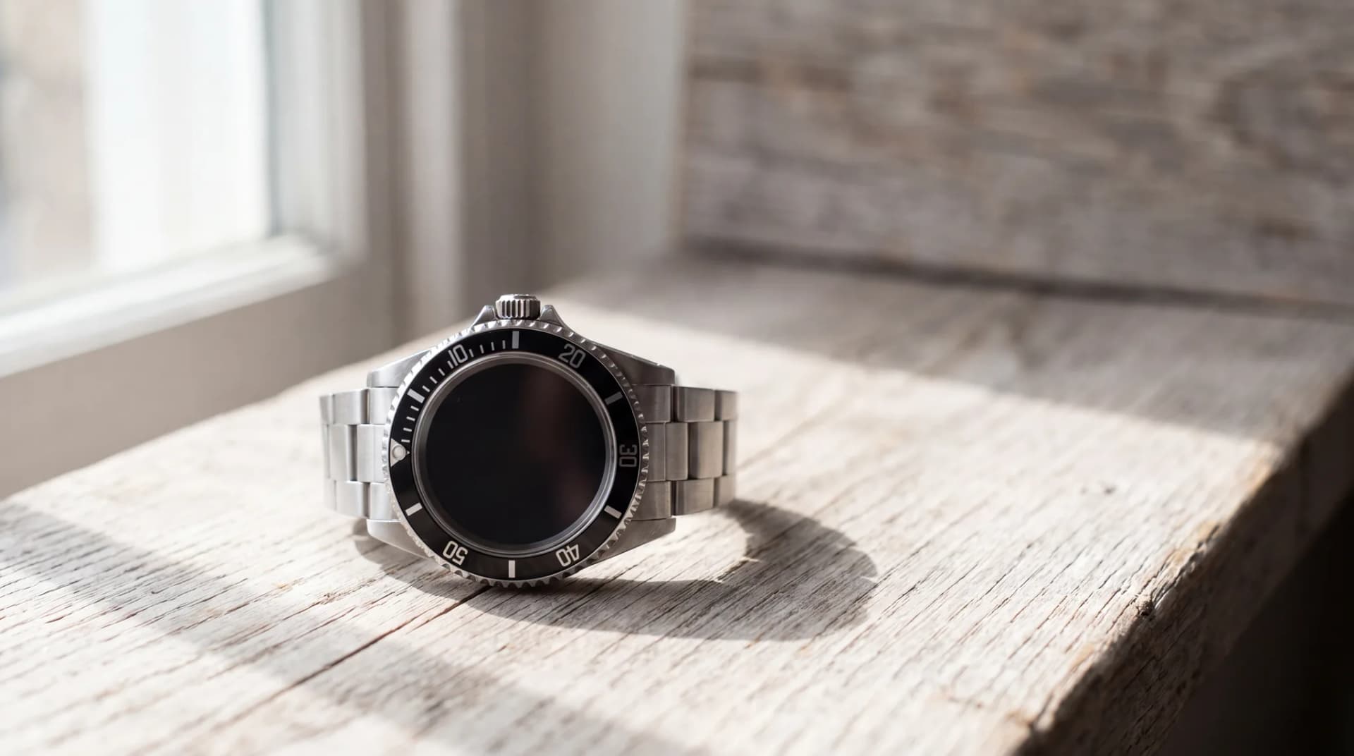 A steel wristwatch with a black numbered bezel, black dial and matching steel bracelet, resting on a pale weathered oak table at ATL Luxury Jewelry, Snellville GA