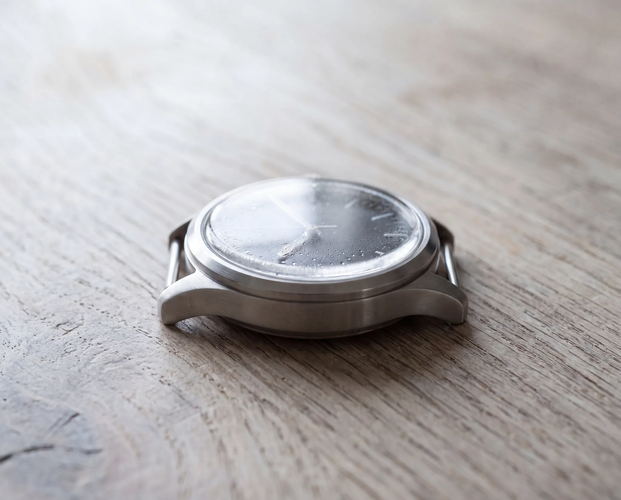 A wristwatch lying on its side on a pale weathered oak table, with condensation beaded on the inside of its crystal at ATL Luxury Jewelry, Snellville GA