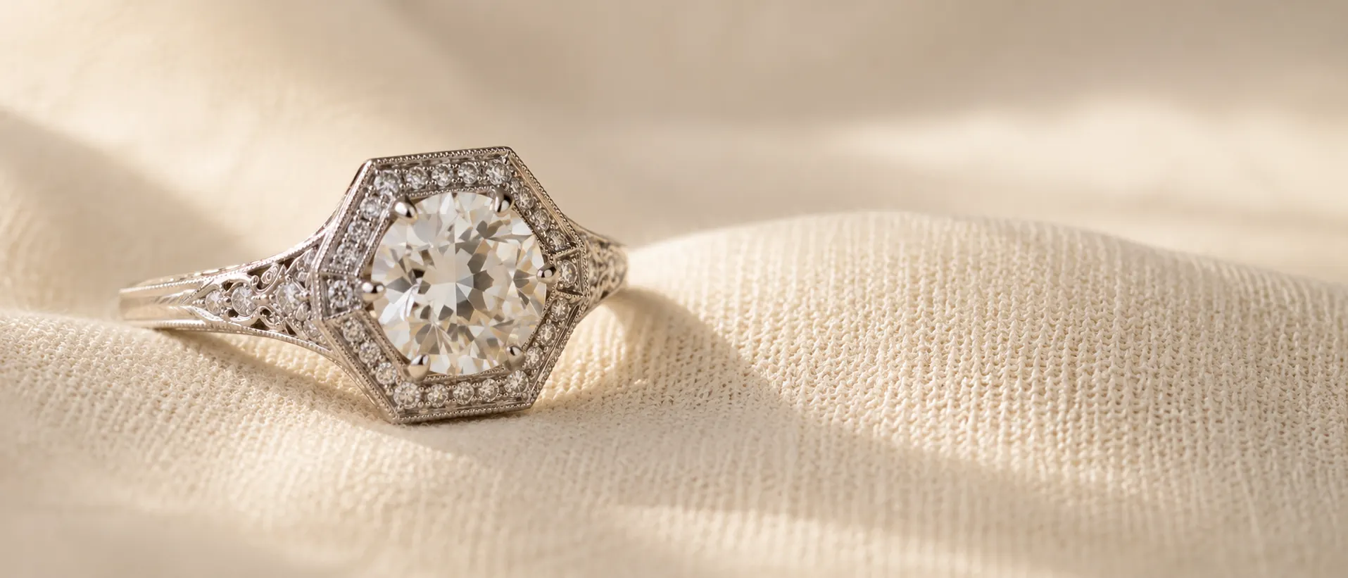 Art Deco engagement ring with hexagonal halo and milgrain on cream linen at ATL Luxury Jewelry Atlanta