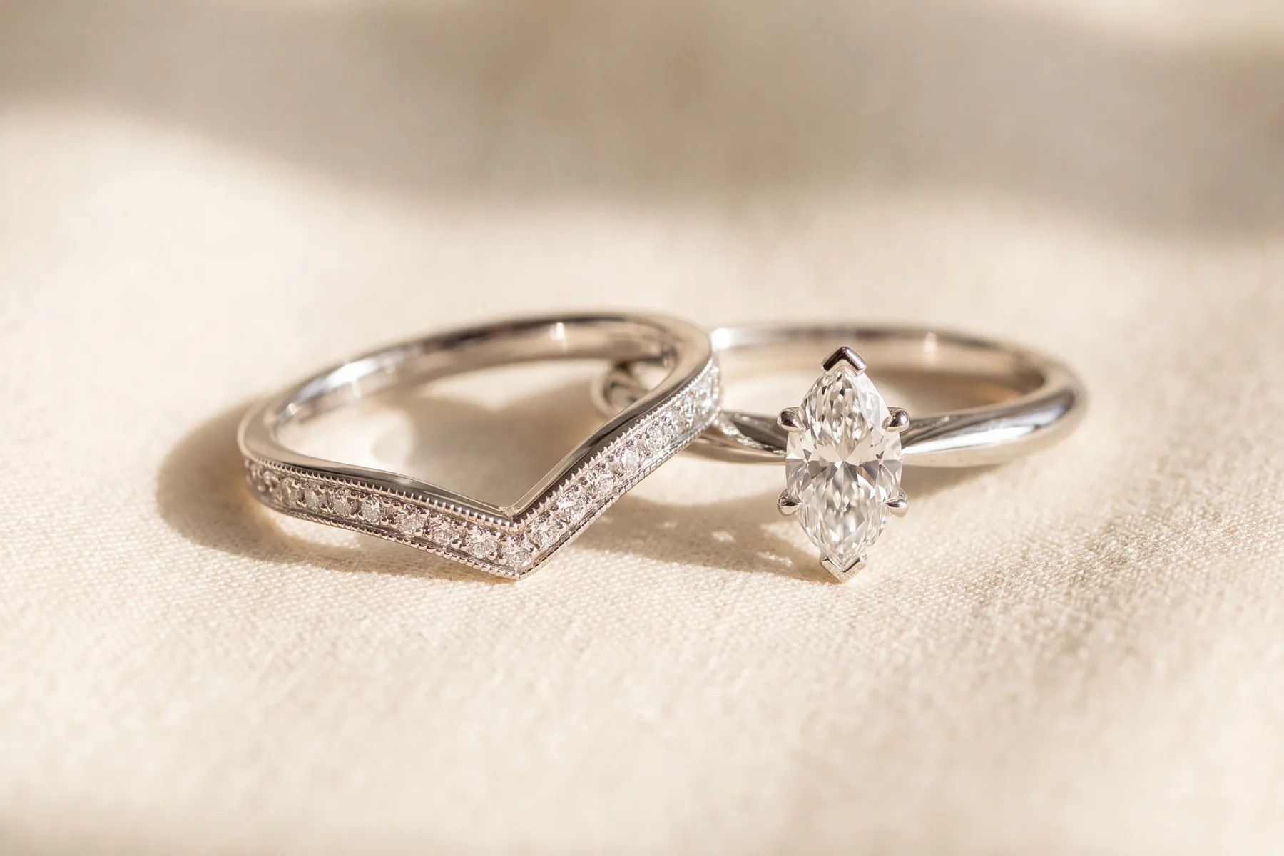 A design study on a cream surface: a white metal band curved in a shallow V so it follows the point of a marquise engagement ring