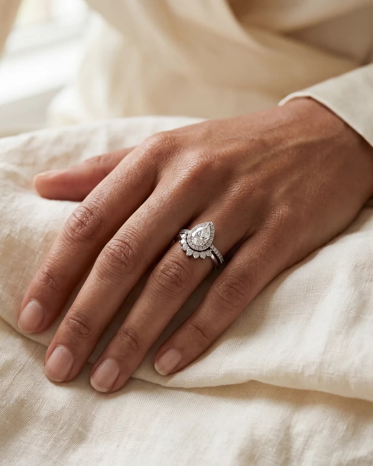 A hand wearing a pear-shaped engagement ring framed by a ring guard, with a band above and below the stone