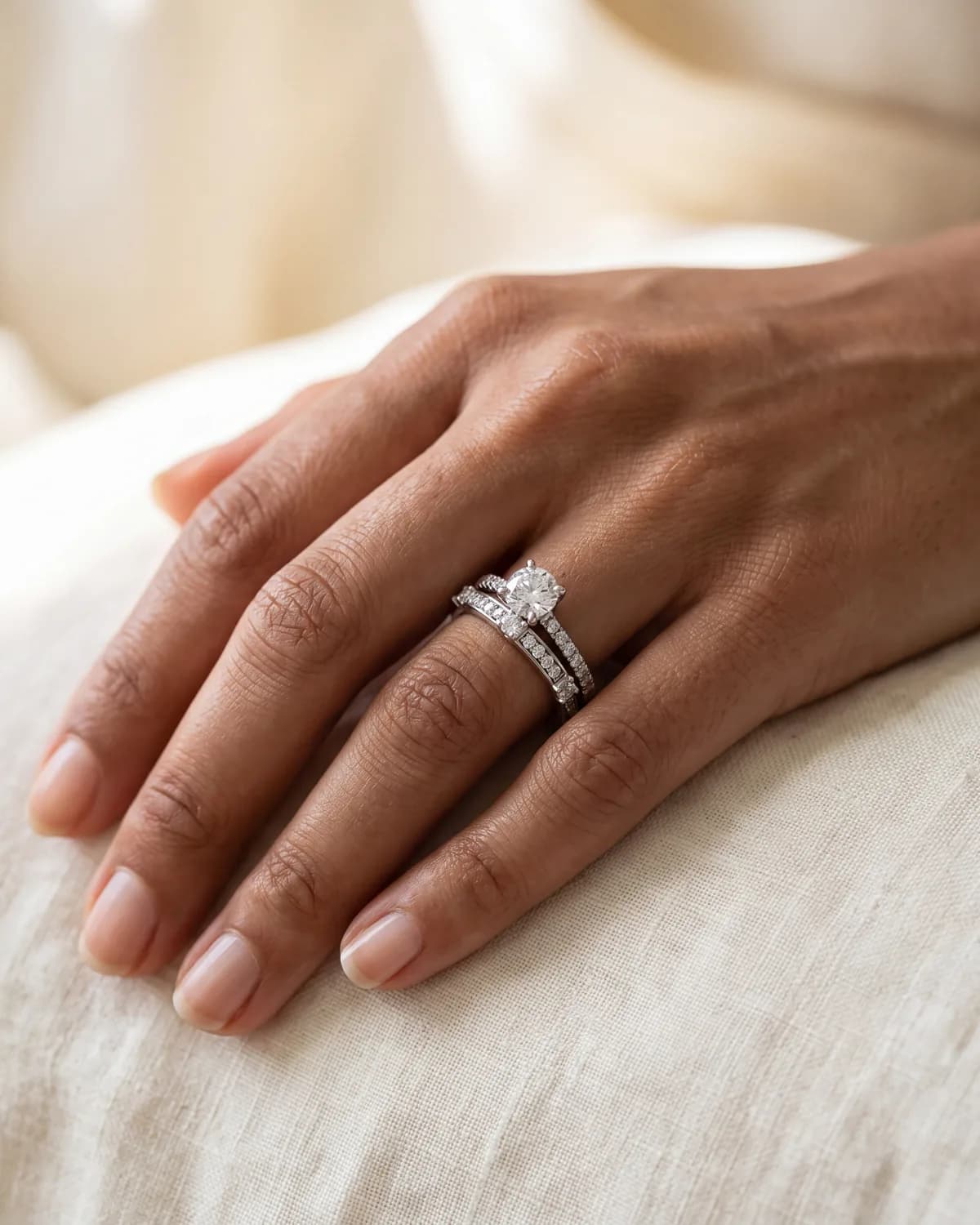 A hand wearing a round solitaire engagement ring with a straight pavé wedding band sitting flush below it