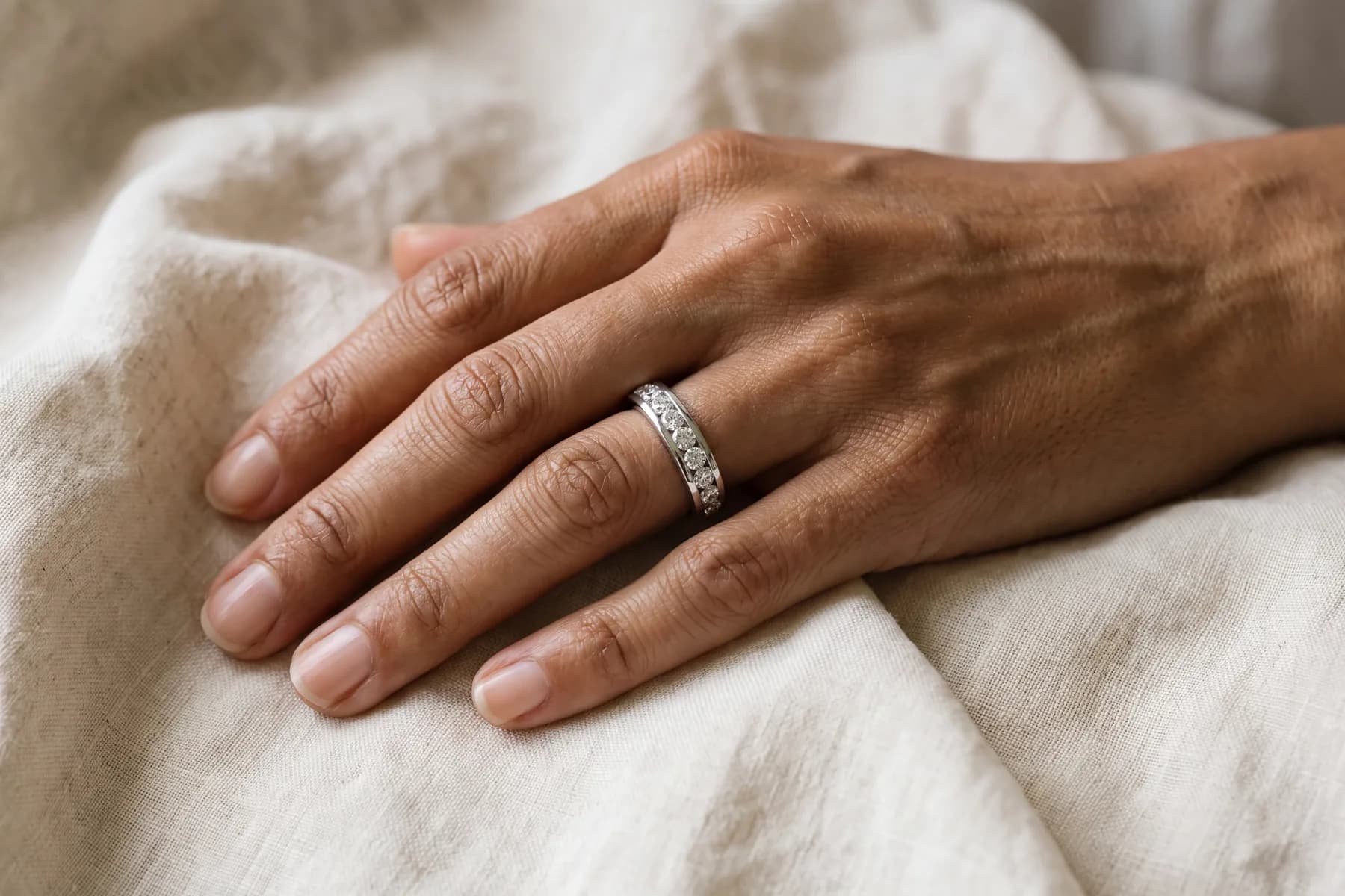 A woman's hand in soft light wearing a diamond wedding band