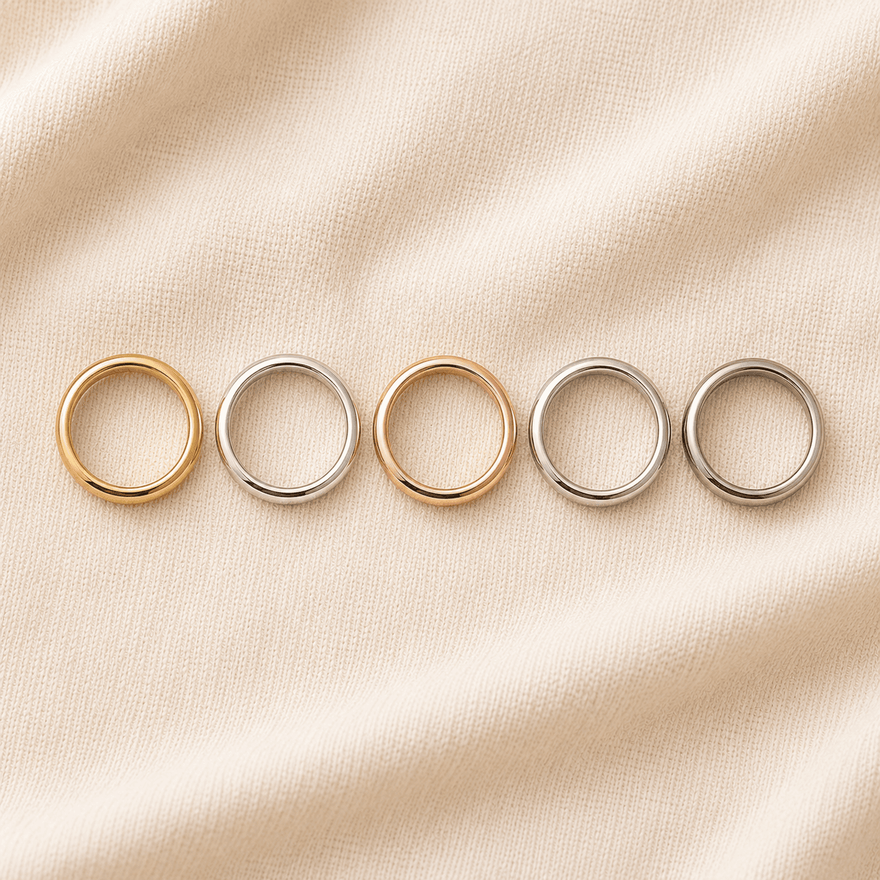 Five wedding bands showing the spectrum of metals — yellow gold, white gold, rose gold, platinum, and palladium — on cream linen at ATL Luxury Jewelers Atlanta