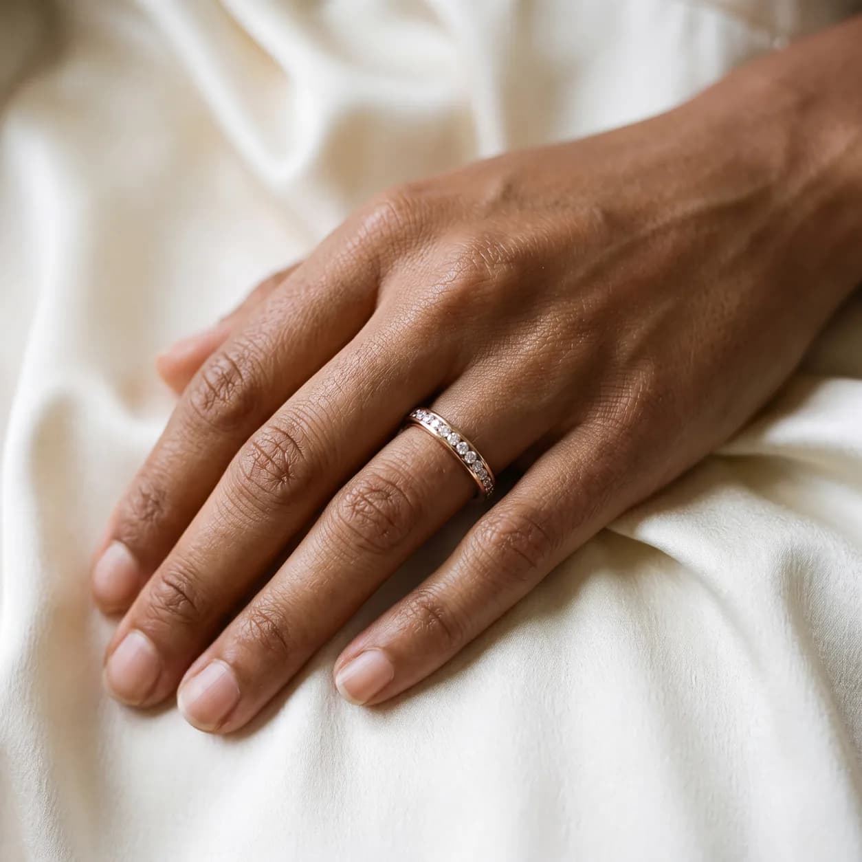 A woman's hand resting on cream linen wearing a thin diamond wedding band, seen close