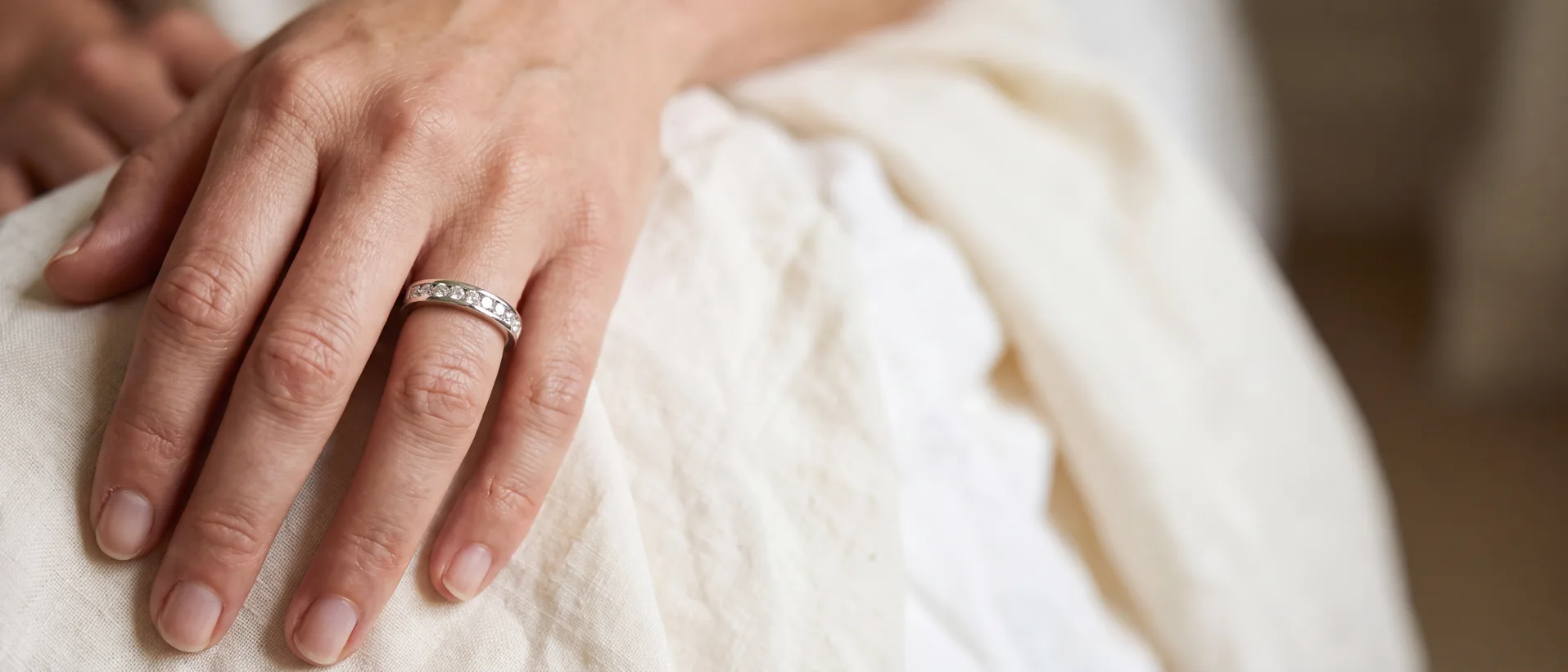 A woman's hand resting on cream linen wearing a thin diamond wedding band